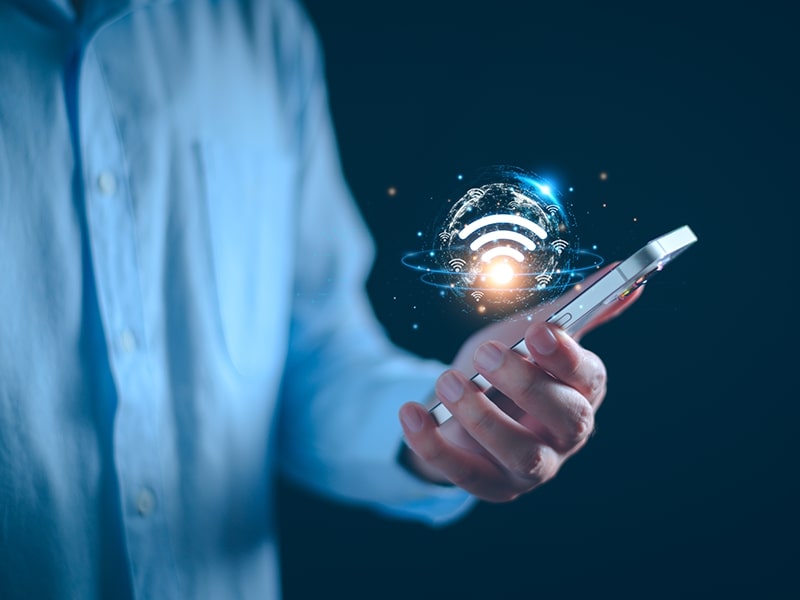 Homem segurando um smartphone com ícone de conexão Wi-Fi flutuando acima, simbolizando a facilidade de acesso à internet em um hotel com WiFi em Foz do Iguaçu. A imagem destaca a importância de uma conexão estável e rápida para os hóspedes que precisam estar conectados durante sua estadia.