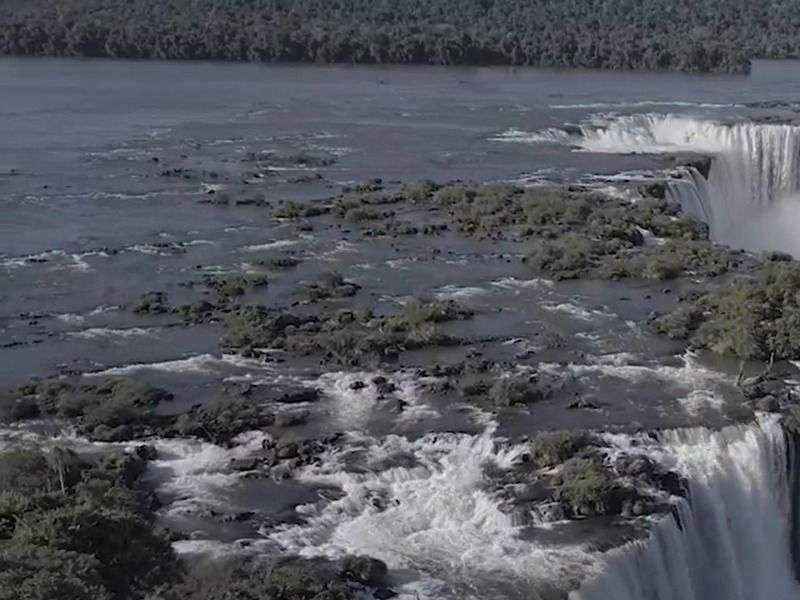 Imagem das quedas d'água no Parque Nacional do Iguaçu, destacando a força das águas que formam as famosas Cataratas do Iguaçu. A imagem revela a vegetação densa ao fundo e a divisão natural das quedas, com o fluxo de água poderoso que caracteriza a Garganta do Diabo, um dos principais atrativos do parque.