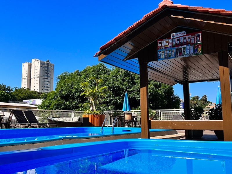 Área de lazer externa de um hotel com piscinas cristalinas, ideal para relaxar sob o céu azul de Foz do Iguaçu. O ambiente inclui espreguiçadeiras e guarda-sóis, proporcionando conforto e tranquilidade aos hóspedes. Este hotel, com as melhores tarifas em Foz do Iguaçu, oferece uma excelente infraestrutura para quem busca momentos de lazer e descanso após explorar as maravilhas da região, como as Cataratas do Iguaçu.