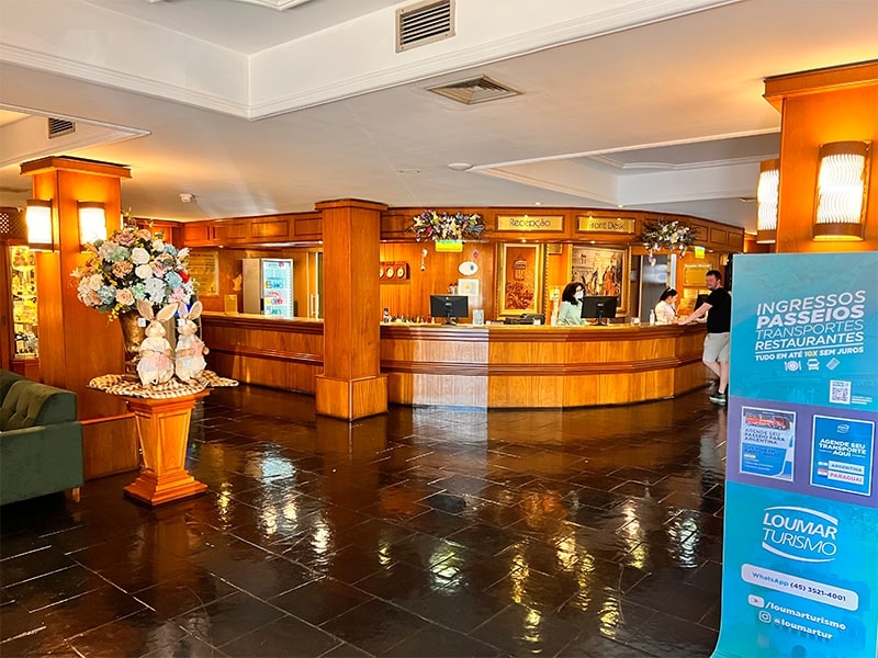 Recepção de um hotel com design aconchegante e decoração elegante, destacando-se por um ambiente acolhedor e bem iluminado. Este hotel com as melhores tarifas em Foz do Iguaçu, proporciona serviços de alta qualidade para quem deseja aproveitar a cidade, com fácil acesso a passeios, transportes e restaurantes locais. Ideal para viajantes em busca de conforto e economia.